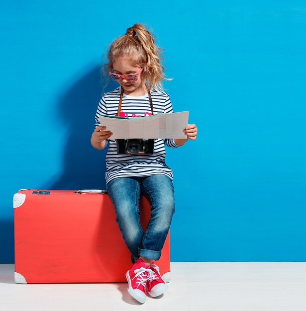 Fille blonde enfant avec valise vintage rose et plan de la ville prêt pour les vacances d'été. Concept de voyage et d'aventure.