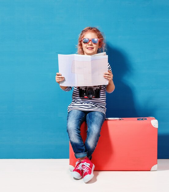 Fille blonde enfant avec valise vintage rose et plan de la ville prêt pour les vacances d'été. Concept de voyage et d'aventure.