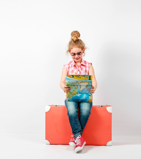 Fille blonde enfant avec valise vintage rose et plan de la ville prêt pour les vacances d'été. Concept de voyage et d'aventure.