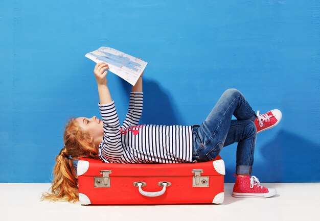 Fille blonde enfant avec valise vintage rose et plan de la ville prêt pour les vacances d'été. Concept de voyage et d'aventure.