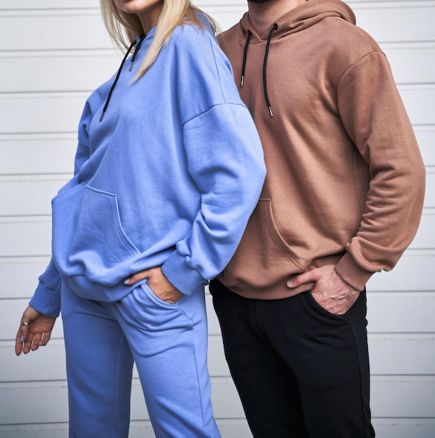 Une fille blonde est debout dans une tenue de sport bleue L'homme porte un sweat à capuche marron et un pantalon noir Le couple porte une tenue assortie à la rue