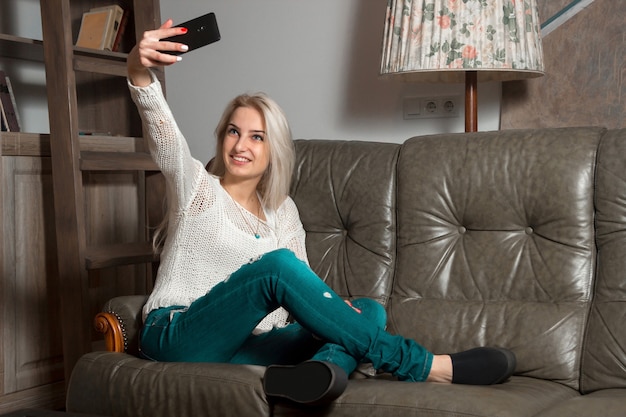 Fille blonde fait selfie avec son téléphone allongé sur le canapé