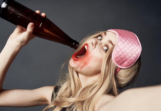 Fille blonde ivre avec une bouteille de bière gestes avec ses mains et un modèle de dépendance au maquillage lumineux