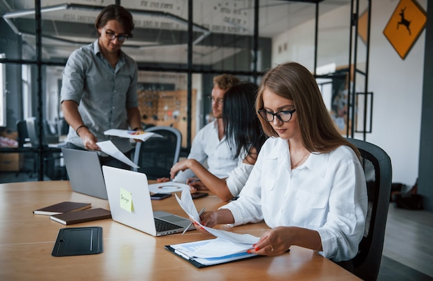 Une fille blonde lit le document. Jeunes gens d'affaires en vêtements formels travaillant au bureau.