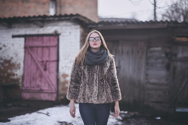 Fille blonde en lunettes de chat yeux dans un manteau de fausse fourrure artificielle posant