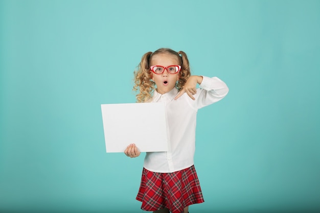 une fille blonde avec des lunettes dans une jupe chemise une écolière tient une feuille de papier blanc dans ses mains