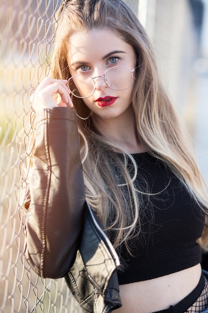 Fille blonde avec des lunettes à la mode posé au coucher du soleil