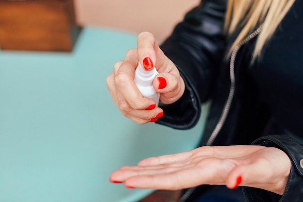 Une fille blonde avec une manucure rouge traite ses mains des germes avec un désinfectant.