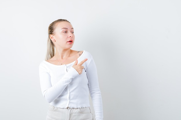 La fille blonde montre son épaule sur le fond blanc