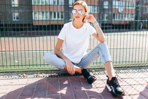 Photo fille blonde portant des t-shirt et des lunettes posant contre la rue