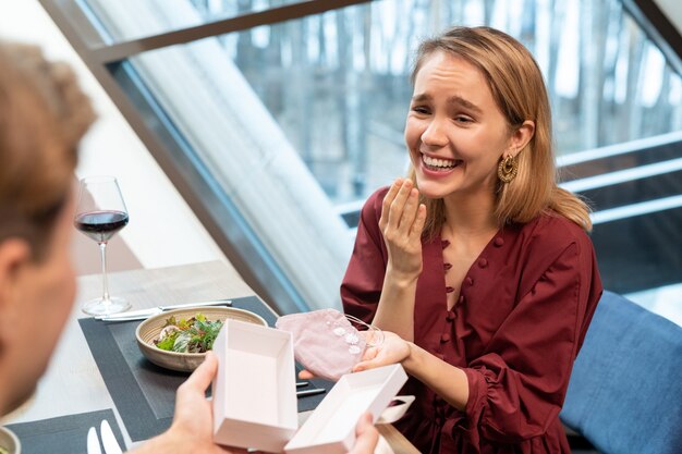 Fille blonde riant à présent de son petit ami et le regardant par le dîner alors que les deux étaient assis à table servie dans un restaurant de luxe