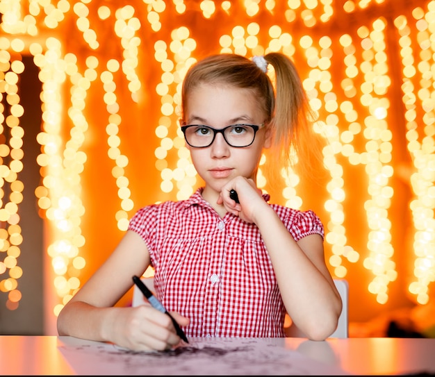 Fille blonde à la robe rose et grandes lunettes noires dessinant le père Noël. Thème de la nouvelle année