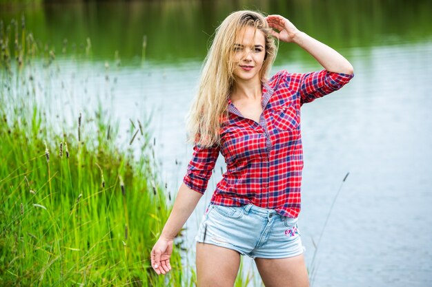 La fille blonde s'amuse dans la rivière en bottes en caoutchouc à la campagne