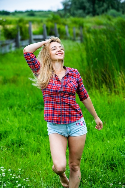 La fille blonde s'amuse dans la rivière en bottes en caoutchouc à la campagne