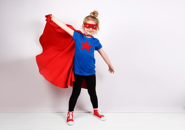 Fille blonde de six ans habillée comme un super-héros s'amusant à la maison. Mur blanc sur fond.