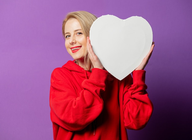 Fille blonde en sweat-shirt rouge tenir coeur