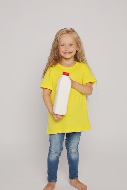 une fille blonde en T-shirt jaune avec une bouteille de lait en plastique dans les mains