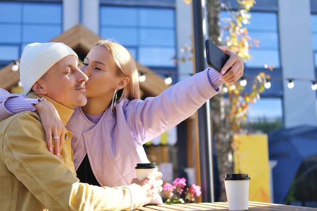 Une fille blonde tient un téléphone et prend un selfie avec son petit ami Fille embrassant un mec