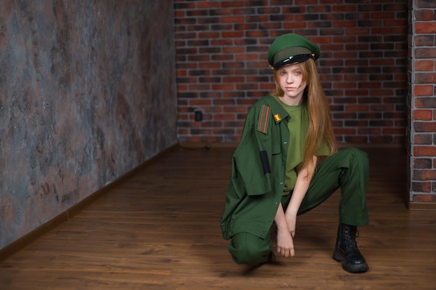 Fille blonde en uniforme militaire et chapeau d'hiver sur le fond d'un mur de briques