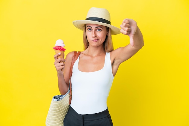 Fille blonde uruguayenne en été tenant de la crème glacée isolée sur fond jaune montrant le pouce vers le bas avec une expression négative