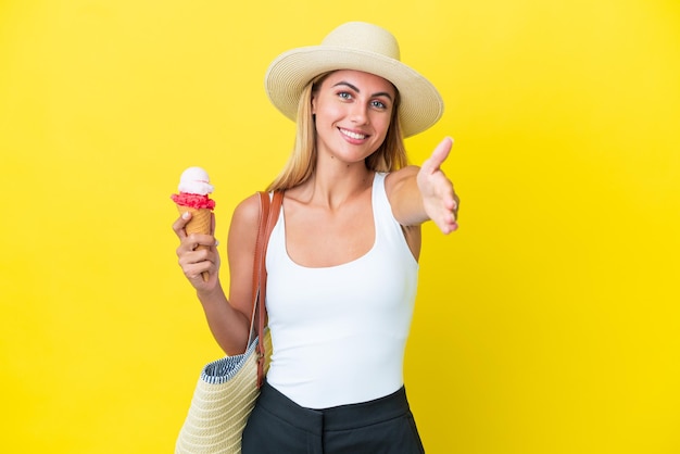 Fille blonde uruguayenne en été tenant de la crème glacée isolée sur fond jaune se serrant la main pour conclure une bonne affaire