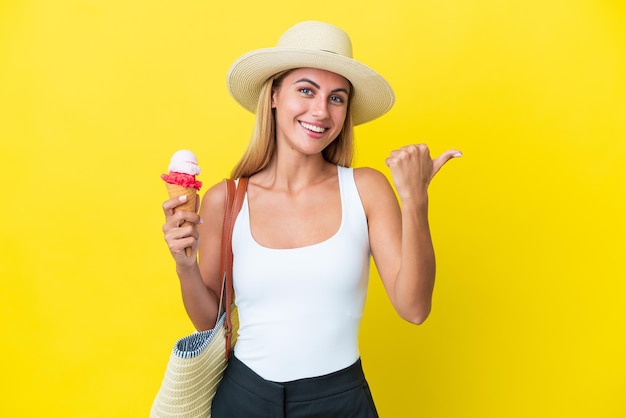 Fille blonde uruguayenne en été tenant une glace isolée sur fond jaune pointant vers le côté pour présenter un produit