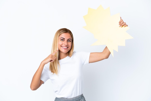 Fille blonde uruguayenne isolée sur fond blanc tenant une bulle vide et la pointant