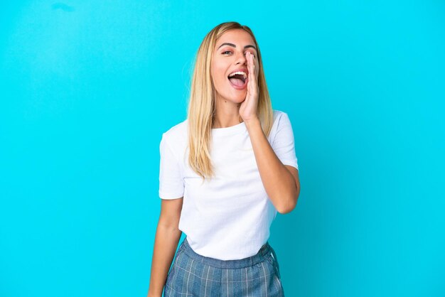 Fille blonde uruguayenne isolée sur fond bleu criant avec la bouche grande ouverte