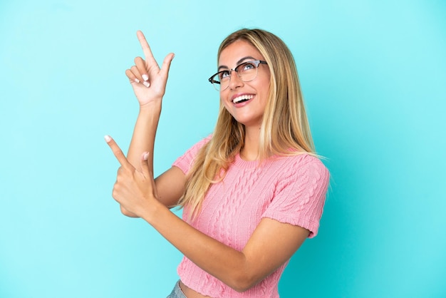 Fille blonde uruguayenne isolée sur fond bleu pointant avec l'index une excellente idée