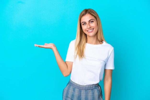 Fille blonde uruguayenne isolée sur fond bleu tenant un fond imaginaire sur la paume pour insérer une annonce