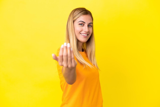 Fille blonde uruguayenne isolée sur fond jaune invitant à venir avec la main Heureux que vous soyez venu