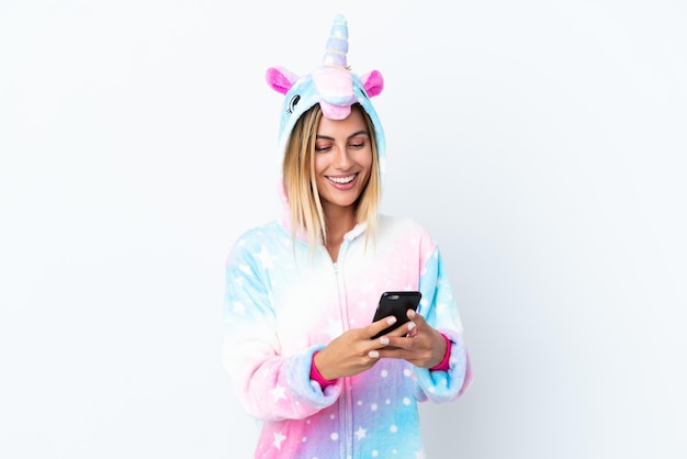 Fille blonde uruguayenne portant un pyjama licorne isolé sur fond blanc en envoyant un message avec le mobile