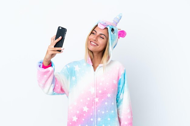 Fille blonde uruguayenne portant un pyjama licorne isolé sur fond blanc faisant un selfie