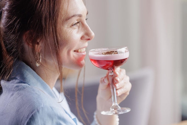 Une fille boit un délicieux cocktail rouge avec de la mousse sur la terrasse d'un restaurant moderne