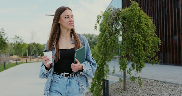 Une fille boit du café en marchant dans la rue avec une tablette