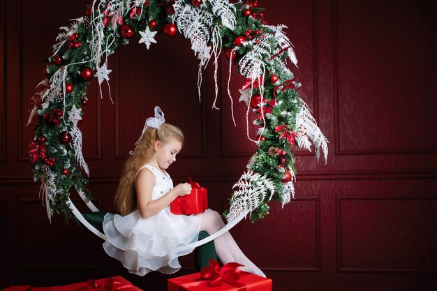 Fille avec la boîte rouge. Cadeau de Noël. L'adolescent est assis sur la balançoire en arc avec des couronnes de décoration du Nouvel An, des branches d'épinette, des boules et des guirlandes.