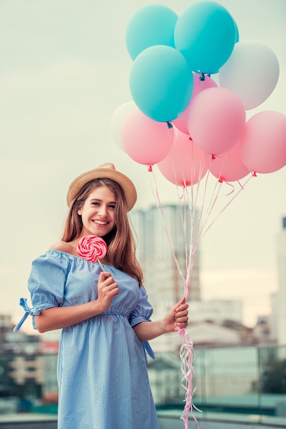 fille avec des bonbons à la main et des boules en souriant. Fille de joyeux anniversaire au chapeau sur la rue.