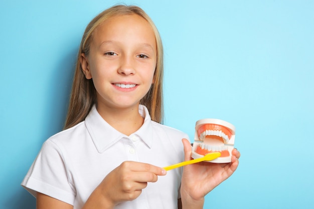 Une fille de bonne humeur se brosse les dents et tient un modèle de dents