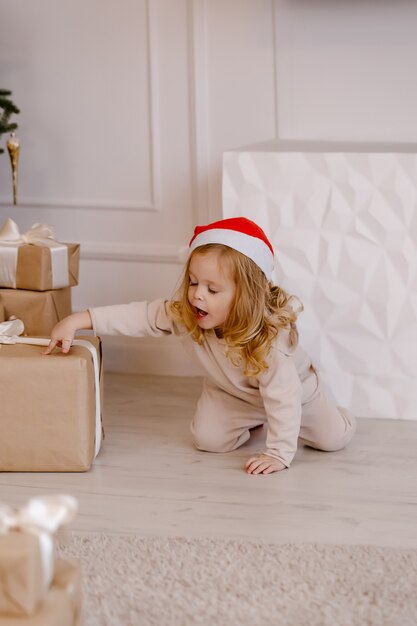 Fille en bonnet de Noel avec cadeau de Noël sous l'arbre de Noël. Enfant avec un cadeau de Noël à la maison.