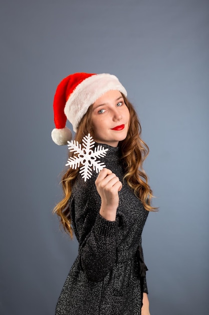 Fille en bonnet de noel portrait avec gros jouet de flocon de neige argenté posant sur fond de couleur grise concept de vacances de Noël heureux et émotions sur fond gris isolé