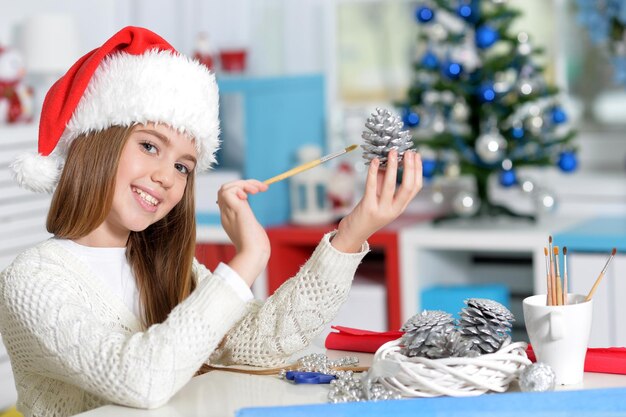 Fille en bonnet de Noel se préparant pour le cône de pin de peinture de Noël