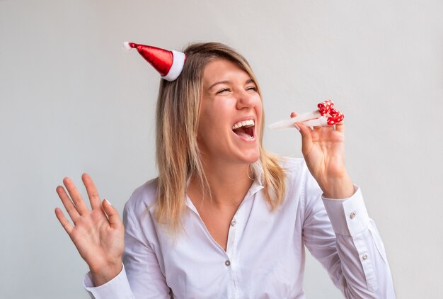 Fille en bonnet de Noel avec le sifflet festif. femme sur espace gris