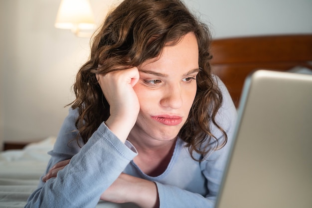 Photo fille bordée allongée sur le lit dans sa chambre en regardant l'ordinateur s'ennuyer femme stressée à l'aide d'un ordinateur portable