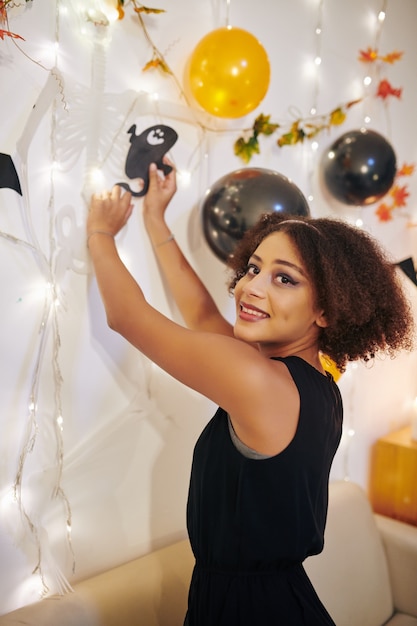 Fille bouclée heureuse avec des murs de décoration de maquillage d'Halloween dans l'appartement pour la fête