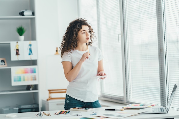 La fille bouclée avec un pinceau dessinant des images sur la table