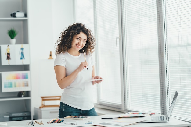 La fille bouclée avec un pinceau dessinant des images sur la table