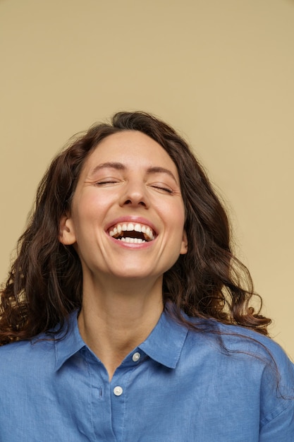 Fille bouclée ravie excitée isolée sur fond beige rire avec la bouche ouverte et les yeux fermés