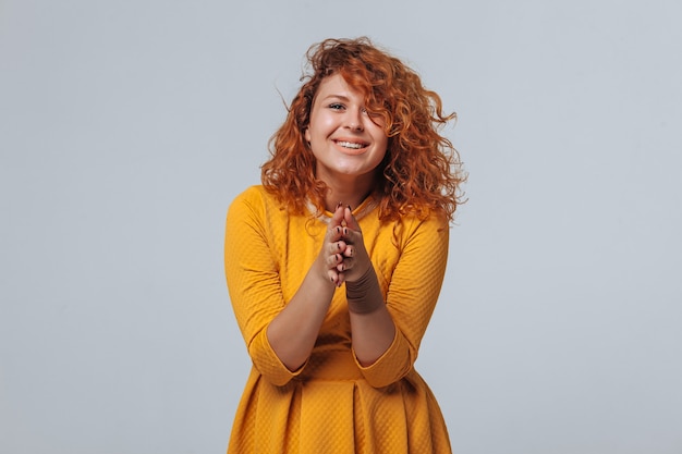 Fille bouclée rouge dans une robe jaune sur fond gris clair souriant