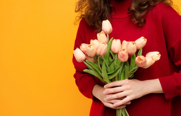 Fille bouclée avec des tulipes en mains isolé sur fond jaune