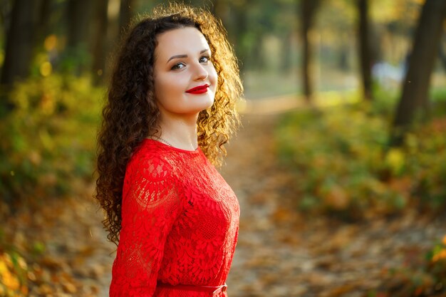 Fille avec des boucles dans une robe rouge dans la forêt d'automne